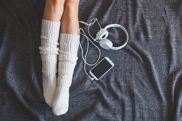 Woman wearing socks to sleep better with headphones and phone