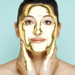 Woman with gold face mask dripping from her skin in front of Tiffany blue background