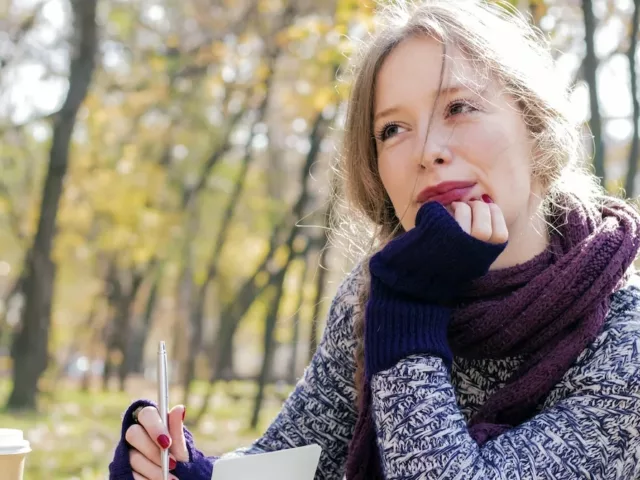 Woman journaling outdoors looking pensive