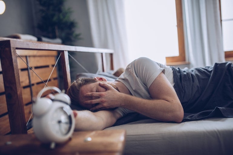 Hungover man in bed who could use milk thistle benefits for liver detox