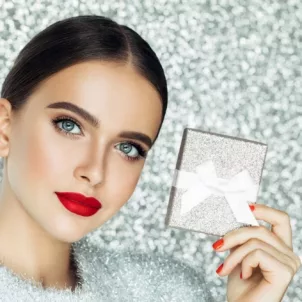 Woman in glam makeup holding a silver gift box over the holidays