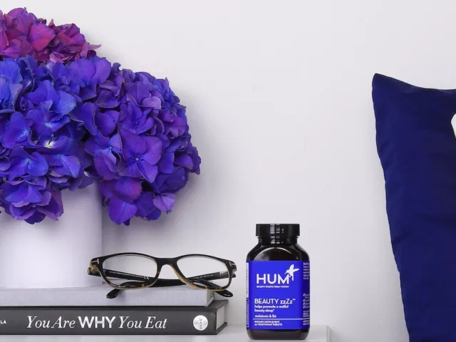 Bottle of HUM Beauty zzZz melatonin supplement on bedside table