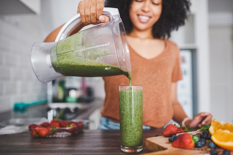 Woman pouring smoothie with chlorella supplement into glass