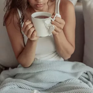 Woman under blanket drinking tea to get rid of her cold