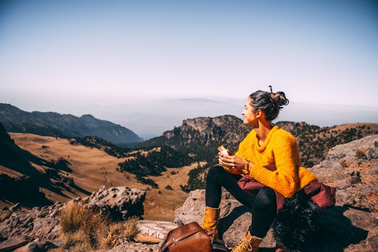 Woman in yellow sweater, calm after taking rhodiola rosea, eating lunch on a hike in the mountains