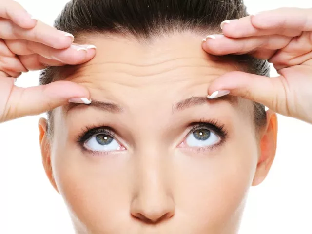 Woman looking up at and holding her wrinkled forehead