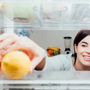 Smiling woman reaching into her fridge for a lemon