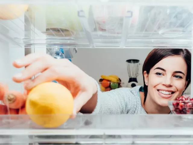 Smiling woman reaching into her fridge for a lemon