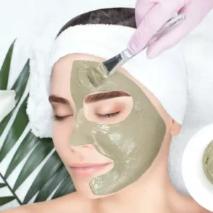 Woman getting a green face mask applied by an esthetician at the spa