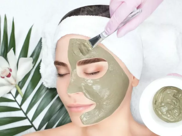 Woman getting a green face mask applied by an esthetician at the spa