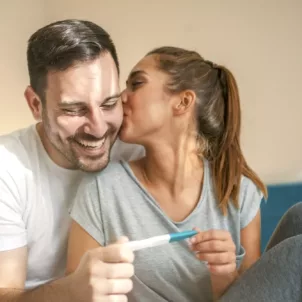 Happy couple in bed with positive pregnancy test; pregnancy tips concept