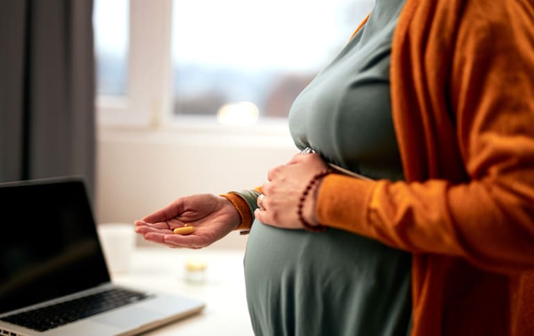 Pregnant woman taking supplements while standing at work