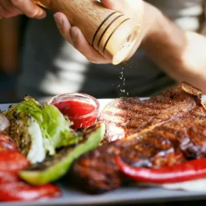 Man cracking black pepper on his steak and grilled veggies on the keto diet