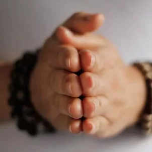 Person wearing mala bracelets with hands clasped together in gratitude