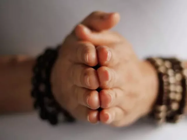 Person wearing mala bracelets with hands clasped together in gratitude