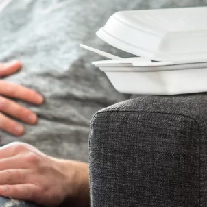 Man on couch touching stomach from pain associated with SIBO