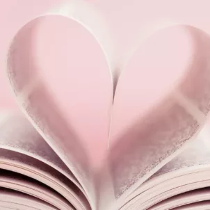 Book pages folded together in a heart shape in front of baby pink background