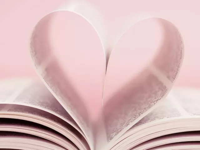 Book pages folded together in a heart shape in front of baby pink background