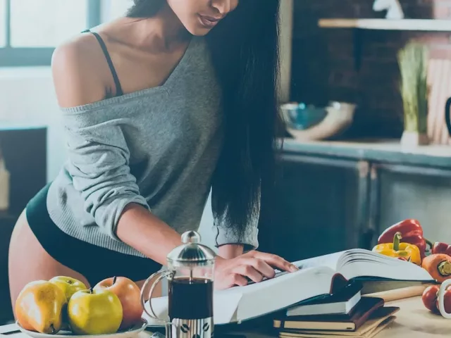 Woman in draped sweater and underwear preparing a meal from a sexy cookbook