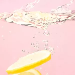 Lemon slices sinking into water on pink background