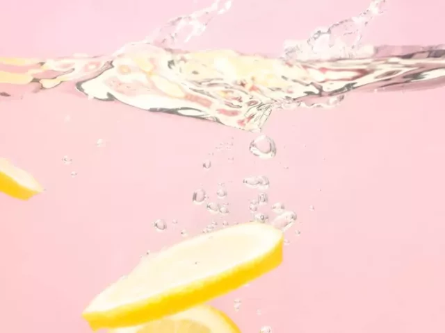 Lemon slices sinking into water on pink background