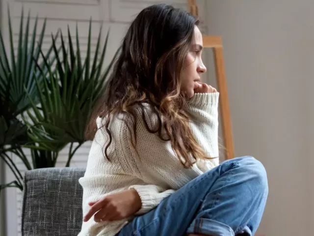 Woman curled into a ball on chair, biting her nails