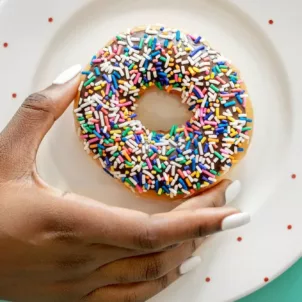 Woman holding a sprinkled chocolate donut, which has unhealthy trans fats