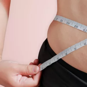 Woman measuring her torso with a tape measure, upset she's in a weight loss plateau