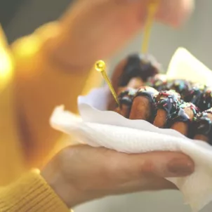 Woman in yellow sweater holding sugary chocolate donuts, which can mess with your gut microbiome