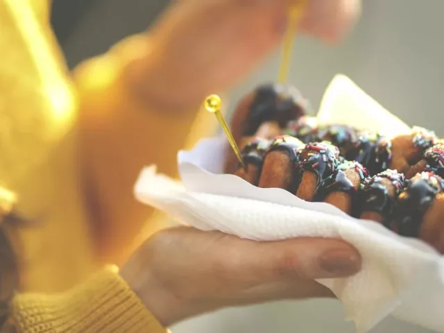 Woman in yellow sweater holding sugary chocolate donuts, which can mess with your gut microbiome