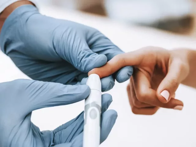 Doctor in gloves checking a woman's triglyceride levels with a finger blood test