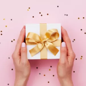 Hands holding a holiday gift with gold bow on pink background