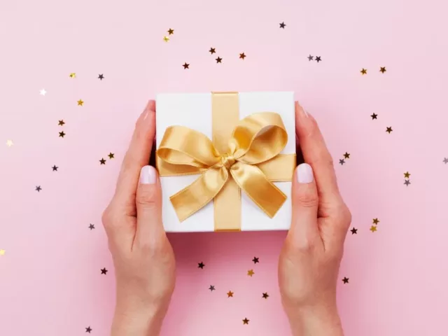 Hands holding a holiday gift with gold bow on pink background