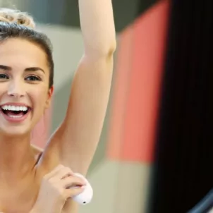 Woman smiling at herself in mirror while applying natural deodorant