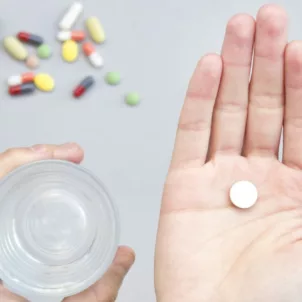 Woman holding a white multivitamin in her palm with a glass of water in the other