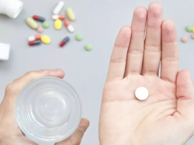 Woman holding a white multivitamin in her palm with a glass of water in the other