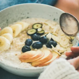 Woman practicing intuitive eating lifestyle with a bowl of oatmeal with fruit slices and berries