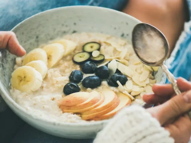 Woman practicing intuitive eating lifestyle with a bowl of oatmeal with fruit slices and berries