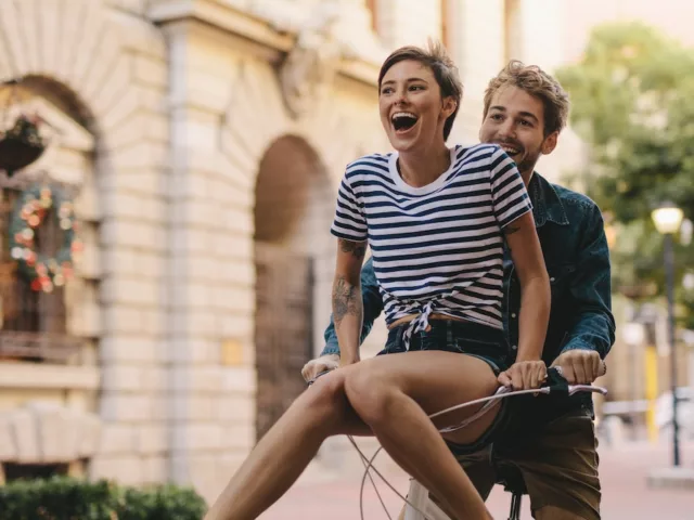 Woman riding on handlebars of her boyfriend's bike