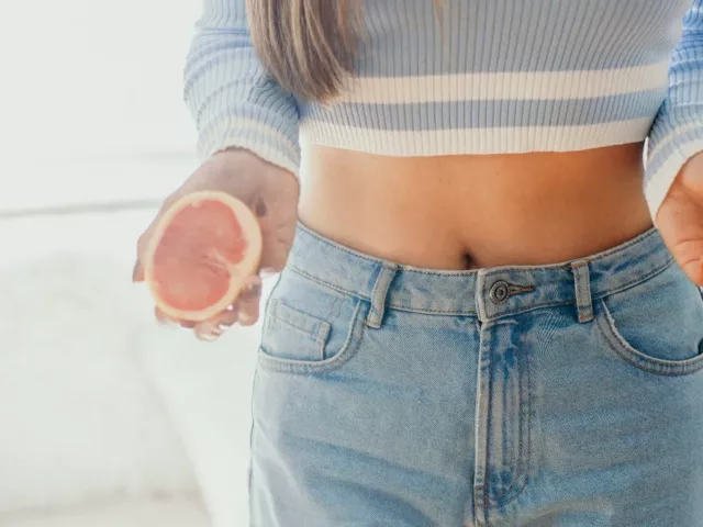 Shot of woman's torso, wearing a cropped sweater and holding an open grapefruit, which boosts metabolism