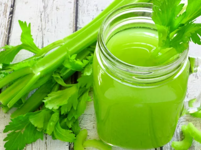 Mason jar for celery juice next to celery stalks on wooden outdoor table