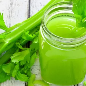 Mason jar for celery juice next to celery stalks on wooden outdoor table