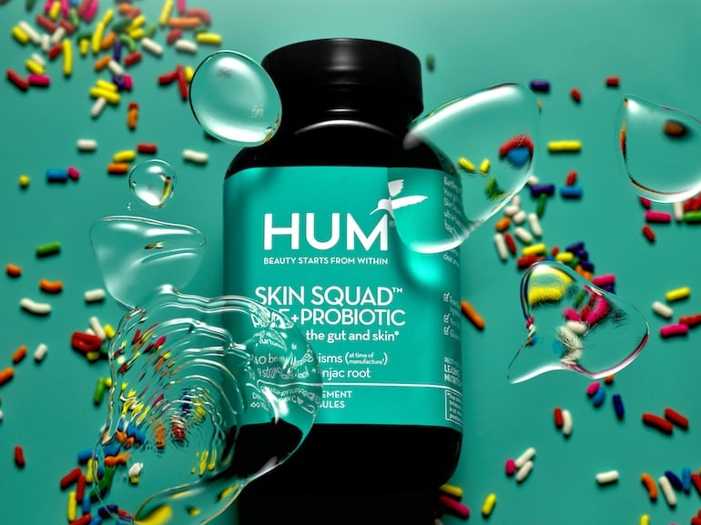 HUM Skin Squad Probiotic for Clear Skin, resting down on green background with rainbow sprinkles and bubbles