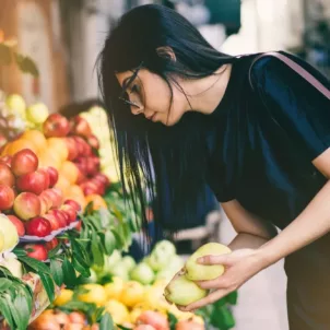 Woman picking fruit outside market on sidewalk