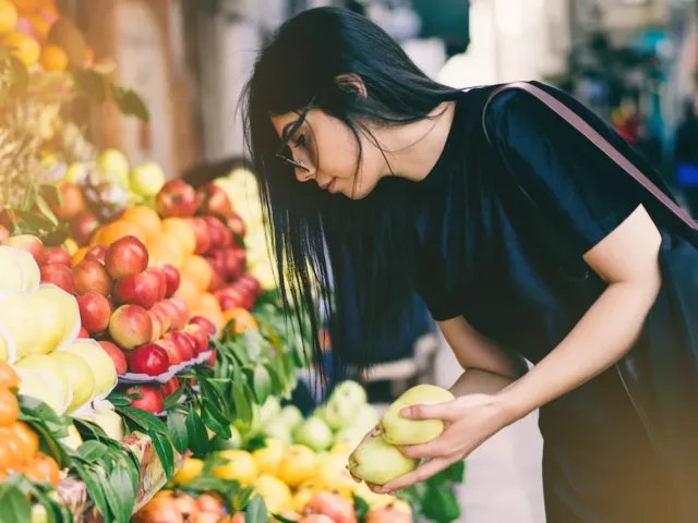 Woman picking fruit outside market on sidewalk