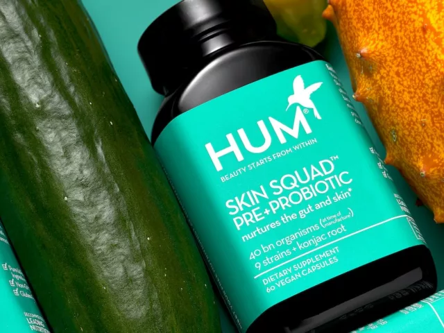 HUM Skin Squad Probiotic supplement for clear skin lined up next to cucumber and other nutritious foods