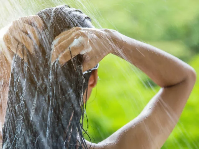 Woman shampooing her hair with best hair care ingredients in outdoor shower