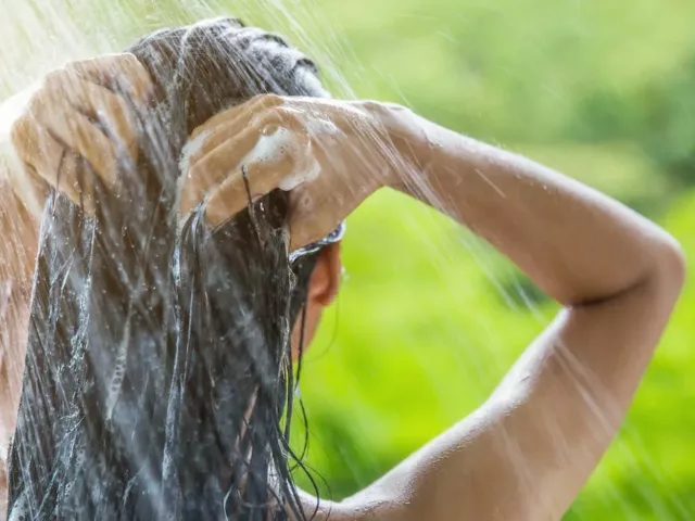 Woman shampooing her hair with best hair care ingredients in outdoor shower