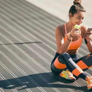 Woman wearing athleisure eating an apple and looking at phone before a workout