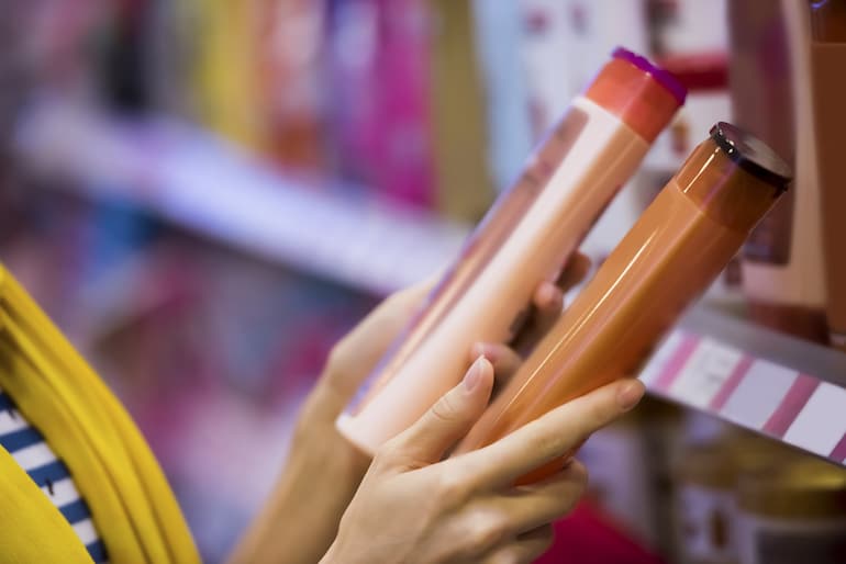 Woman holding up two shampoo bottles comparing labels and ingredients